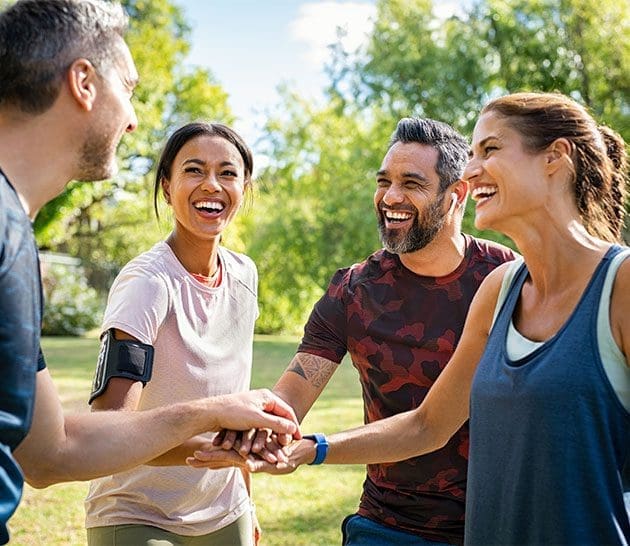 group of four adults, two women and two men, huddled in a circle, smiling and talking