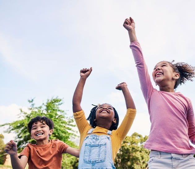 three children smiling with their arms in the air