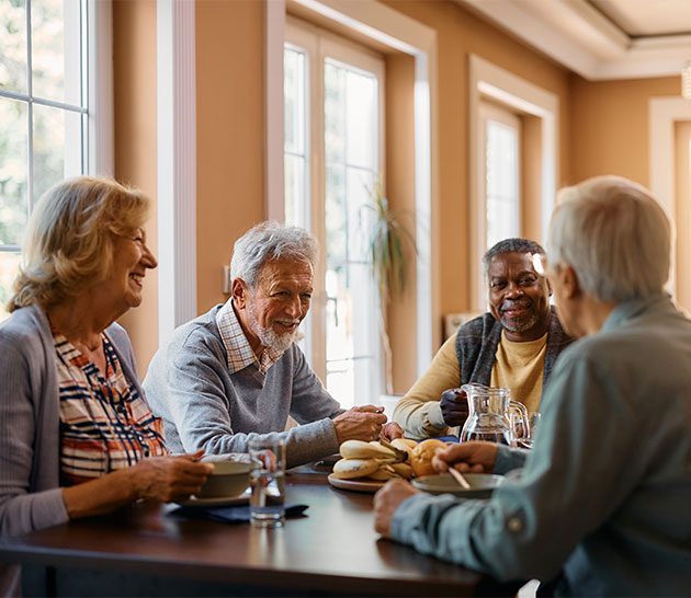 table with four senior citizens sitting at it, smiling and talking