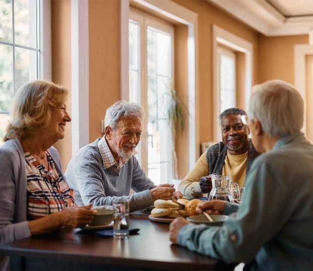 table with four senior citizens sitting at it, smiling and talking