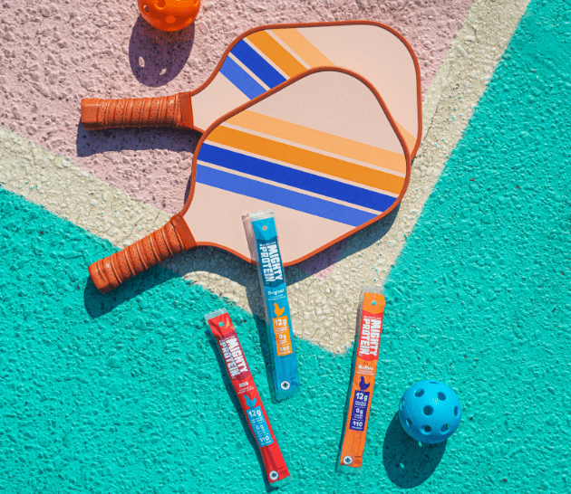 Mighty Protein products on a pickleball court with paddles.