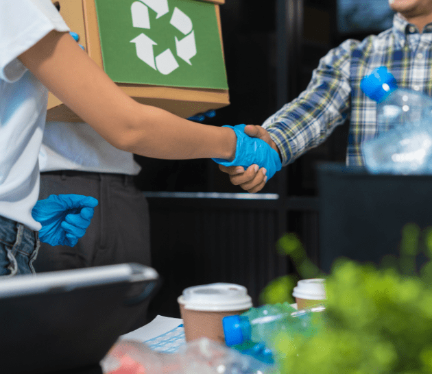 Two people shaking hands while sorting through recycling.